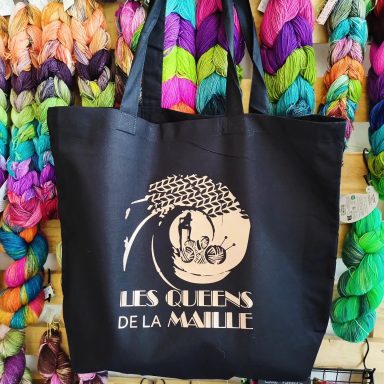 Sac en toile noir avec le texte "Les Reines de la Maille" et un motif de pelotes de laine.