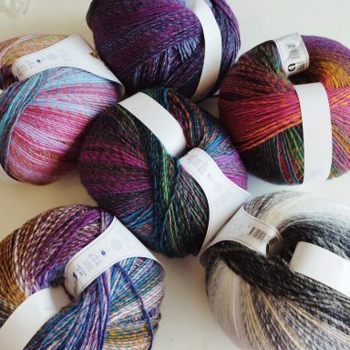 Pelotes de laine de différentes couleurs, disposées en cercle sur une surface claire.