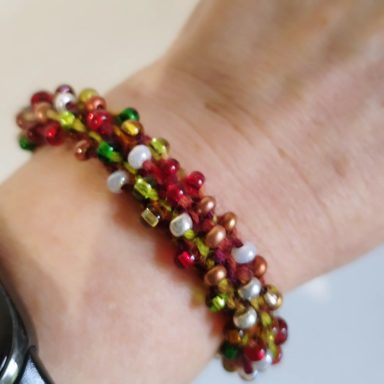 Bracelet coloré avec des perles rouges, dorées, vertes et blanches enroulé autour d'un poignet.